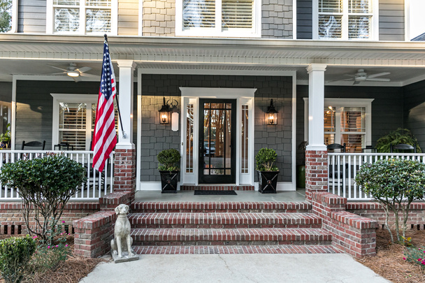 Puerta de entrada a una gran casa de dos pisos gris azul con revestimiento de madera y vinilo y una gran bandera estadounidense. - Foto, imagen