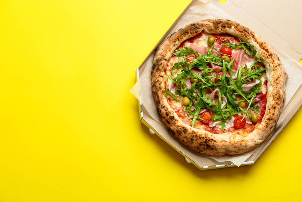 Tasty pizza with meat and arugula in cardboard box on yellow background, top view. Space for text - Fotografie, Obrázek