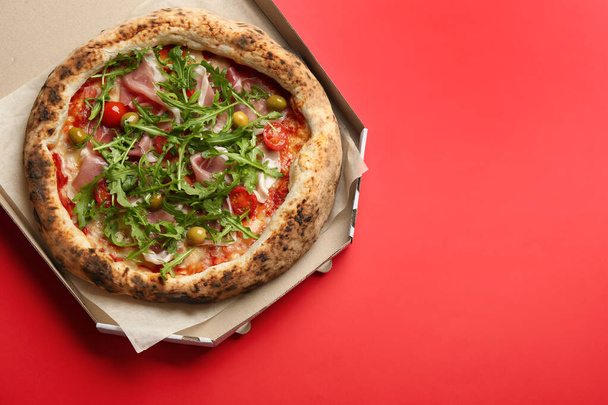 Tasty pizza with meat and arugula in cardboard box on red background, top view. Space for text - Photo, image