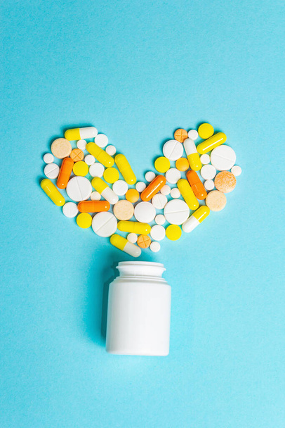 Assorted pharmaceutical medicine pills, tablets and capsules for the treatment of heart disease. Heart shape and bottle of pills. Gradient blue background, copy space for text - Photo, Image