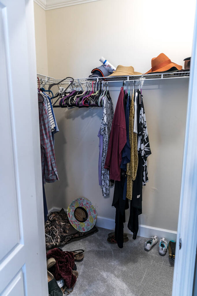 A mostly empty walk in messy closet with some hanging clothes and hats - Photo, Image