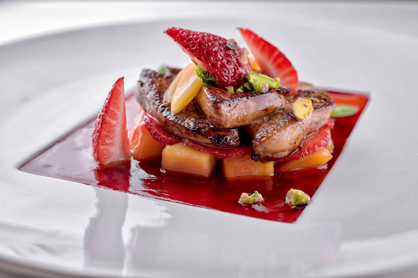 Foie gras in strawberry sauce with pear and strawberry pieces on white plate - Foto, Imagen