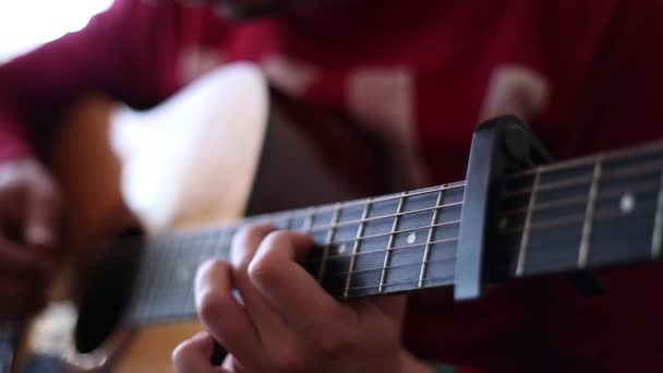 Ein Mann im roten Pullover spielt drinnen eine Akustikgitarre, eine Nahsicht auf eine weit geöffnete Blende - Filmmaterial, Video