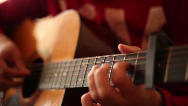 Um homem com uma camisola vermelha toca uma guitarra acústica dentro de casa, uma visão de perto de uma ampla abertura aberta - Filmagem, Vídeo