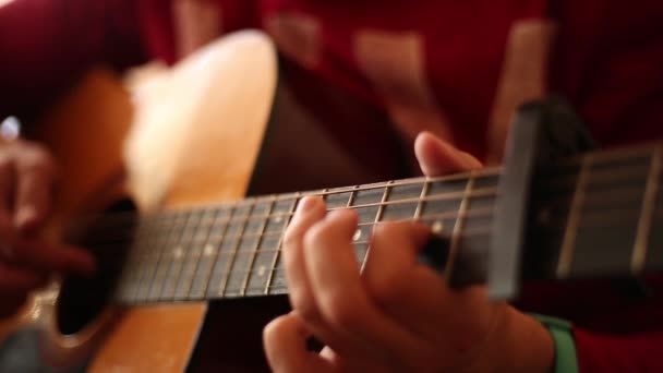 赤いセーターを着た男が室内でアコースティックギターを演奏し、広い開口部のクローズアップを再生します。 - 映像、動画