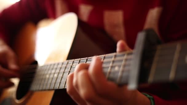 Een man in een rode trui speelt binnen een akoestische gitaar, een close-up van een wijd open diafragma - Video