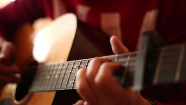 Ein Mann im roten Pullover spielt drinnen eine Akustikgitarre, eine Nahsicht auf eine weit geöffnete Blende - Filmmaterial, Video