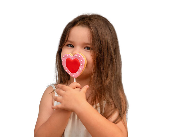 Το κορίτσι με τα μπισκότα καρδιάς απομονώνεται. Παιδί που κρατά γλυκύτητα σε ένα ραβδί στο λευκό - Φωτογραφία, εικόνα