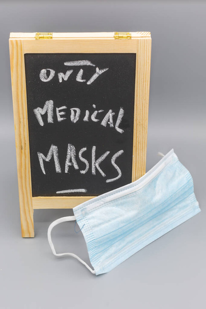 Tableau noir de dessus oblique avec avertissement seulement des masques médicaux et un masque de chirurgie bleue au premier plan. Vertical - Photo, image
