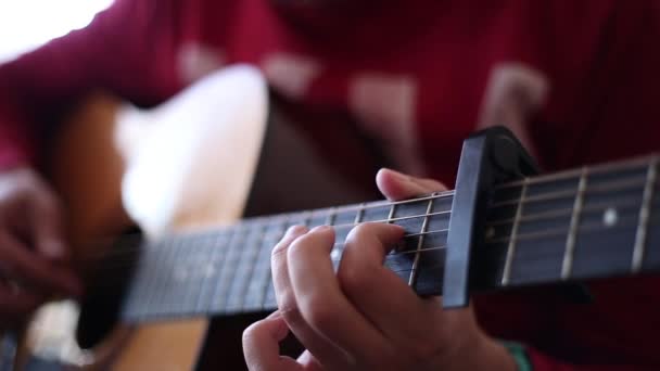 Mężczyzna w czerwonym swetrze gra na gitarze akustycznej wewnątrz, z bliska widok szerokiej otwartej apertury - Materiał filmowy, wideo