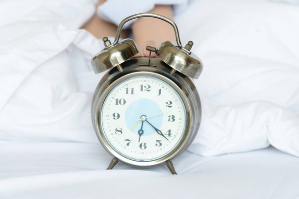 Alarm clock silver style vintage place on a bed with hands of woman holding a clock. retro analog watch on white bed in morning time. 6 o'clock with copy space.Getting enough sleep concept. - Photo, Image