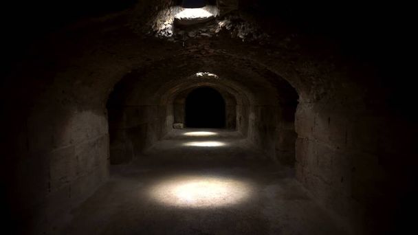 Περνώντας από ένα σκοτεινό ρωμαϊκό υπόγειο. Υπόγειο κάτω από το Αμφιθέατρο στο Ελ Τζεμ της Τύνιδας. Αρχαίο ρωμαϊκό κτίριο. Η κάμερα απομακρύνεται. - Φωτογραφία, εικόνα