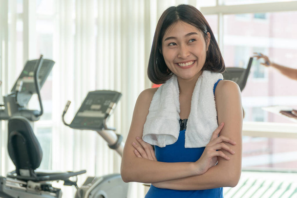 Portret van een vrolijke sportvrouw met staande armen gekruist in fitness gym.Mooie vrouw met blauwe sportkleding vrolijk lachend in de sportschool voor elliptische toestellen. - Foto, afbeelding