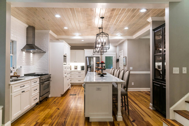 Large renovated white kitchen with textured subway tile, black iron lights and pine hardwood flooring - Photo, Image