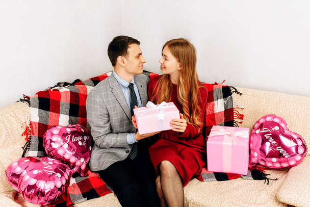 Young couple in love holding gifts for Valentine's Day sitting on sofa at home, hugs, love concept for Valentine's Day, Women's Day - Fotografie, Obrázek