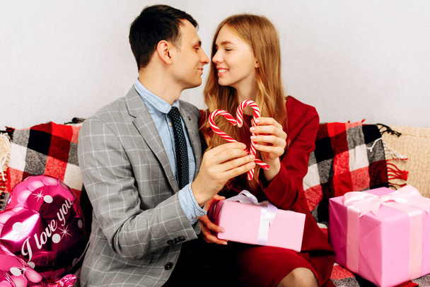 Young couple in love holding gifts for Valentine's Day sitting on sofa at home, hugs, love concept for Valentine's Day, Women's Day - Foto, imagen