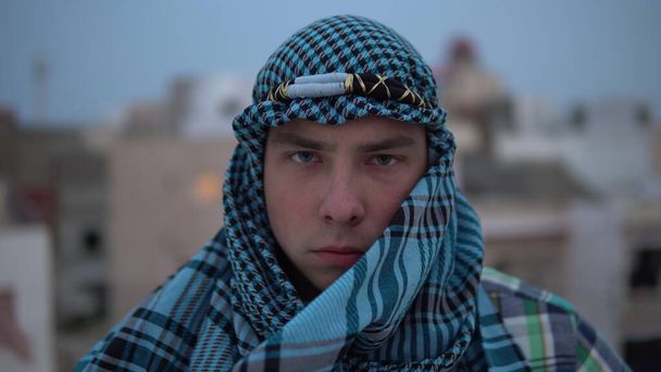 Een jongeman in een Arabische zakdoek. De man kijkt naar de camera. Op het dak van een huis tegen de achtergrond van Arabische huizen. - Foto, afbeelding