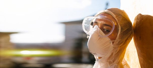 Banner. A tired doctor in protective medical equipment and goggles looks at the camera against the backdrop of the bright sun during outdoor break between a hard fight with covid 19. - 写真・画像