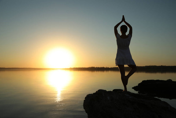 Woman practicing yoga near river on sunset. Healing concept - 写真・画像