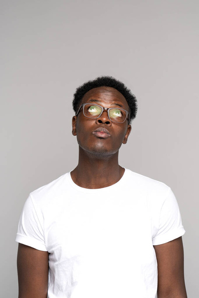 Αφροαμερικάνος με γυαλιά φοράει λευκό t-shirt σκεπτόμενος, κοιτάζοντας ψηλά στο χώρο αντιγραφής, απομονωμένος - Φωτογραφία, εικόνα