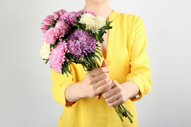 Woman with bouquet of beautiful asters on light background, closeup. Autumn flowers - Фото, изображение