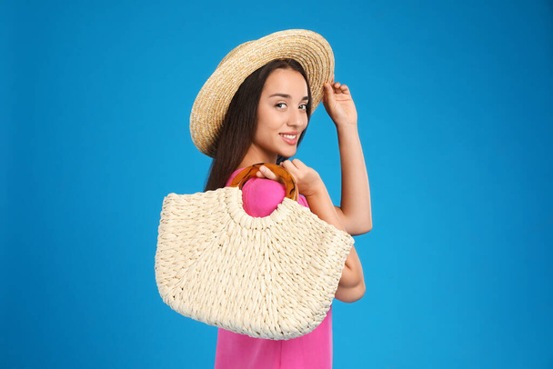Young woman with stylish straw bag on light blue background - Zdjęcie, obraz