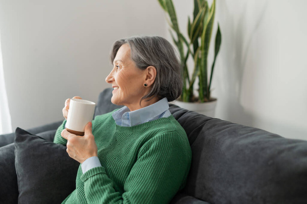 Senior lady enjoying a hot drink in the living room - Foto, Imagen