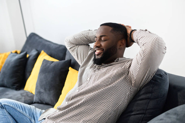 Relaxed smiling Afro American enjoying life sitting on the sofa - Fotó, kép