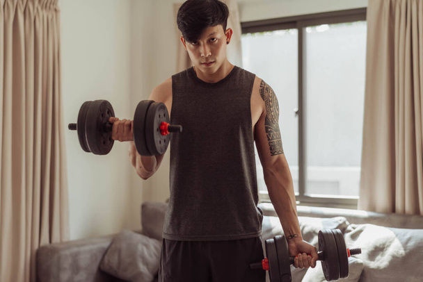Fit man doing arms exeise at home. Young man doing biceps curl with dumbbells in living room at home. - Foto, imagen