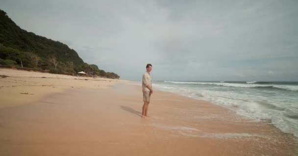 Dollit lelőtték, amint egy fiatal khaki ruhás férfitól távolodott, aki a Bali-i tengerparton állt a hullámokban. - Felvétel, videó