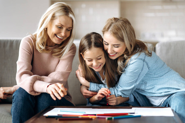Weekend leisure. Cheerful caucasian happy grandmother daughter and granddaughter spend time at home together, drawing with pencils in living room, hugging and laughing - Φωτογραφία, εικόνα