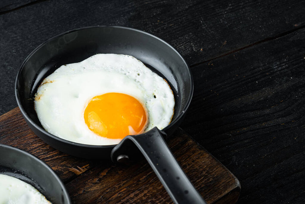 Fried eggs with bacon and vegetables set in cast iron frying pan, on black wooden table background , with space for text copyspace - Photo, Image