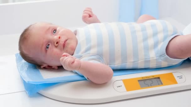 Крупный план 1-месячного новорожденного мальчика лежащего на цифровых весах или весах. Концепция младенцев и гигиены новорожденных и здравоохранения. Заботливые родители с маленькими детьми. - Кадры, видео