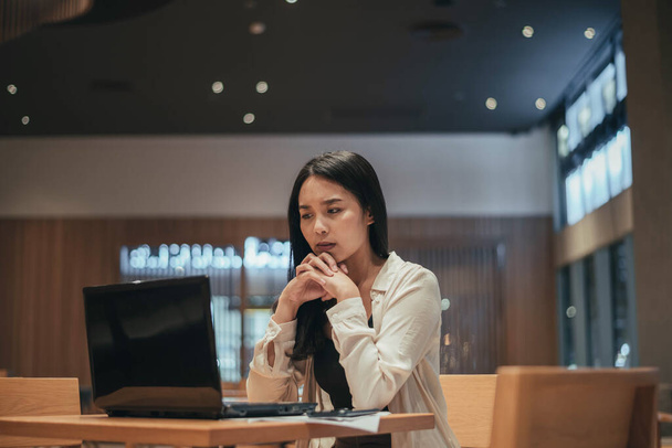 Una mujer seria trabajando en un portátil tarde en la noche. Asiática empresaria trabajando duro y horas extras en la oficina. - Foto, imagen