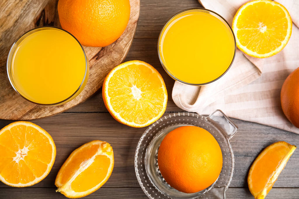 Fresh ripe oranges, squeezer and juice on wooden table, flat lay - Φωτογραφία, εικόνα