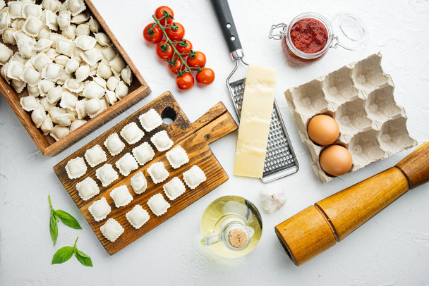 Ωμό ιταλικό ραβιόλι tortellini με φρέσκια παρμεζάνα και βασιλικό, ντομάτες σε ξύλινη σανίδα, σε λευκό φόντο, πάνω όψη επίπεδη lay - Φωτογραφία, εικόνα
