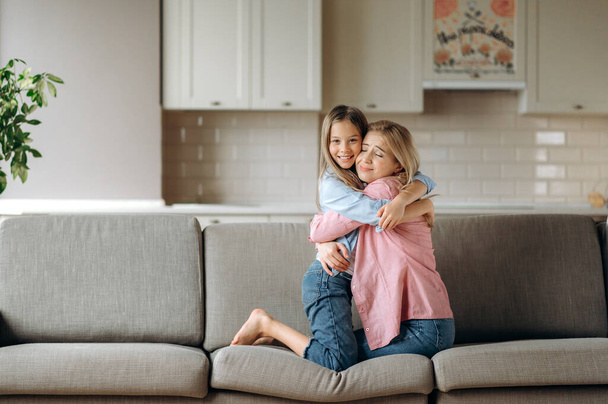 Prawdziwa miłość matki i córki. Zmysłowy portret uroczej białej mamy i córki przytulających się delikatnie na kanapie w domu i uśmiechających się. Szczęśliwi razem - Zdjęcie, obraz