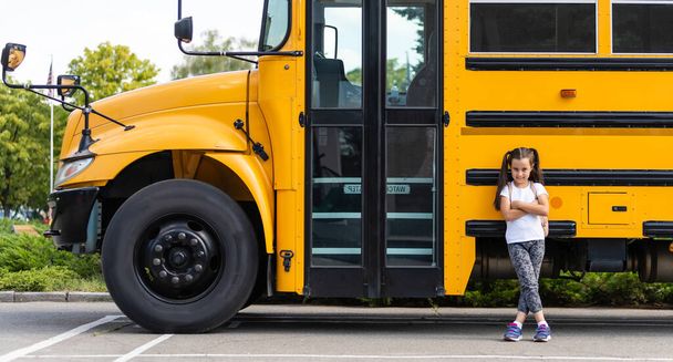 Nettes Mädchen mit einem Rucksack, das in der Nähe des Busses steht und zur Schule geht, posiert nachdenklich vor der Kamera in Nahaufnahme - Foto, Bild