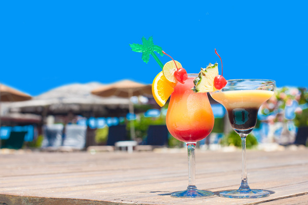 Two glasses of bright cocktails near pool on clear blue sky background - 写真・画像
