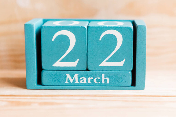 22 mars. Calendrier cube bleu avec mois et date sur fond bois. - Photo, image