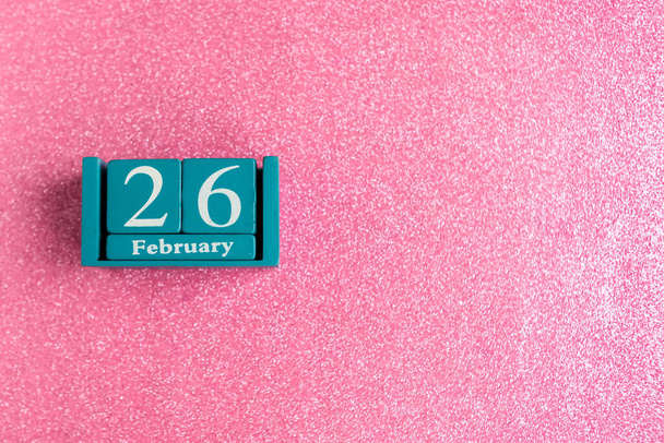 26 febbraio. Calendario blu cubo con mese e data su sfondo rosa glitter. Copia lo spazio per il testo - Foto, immagini