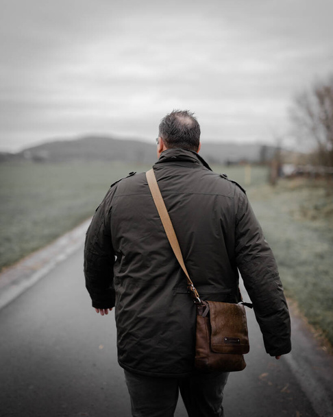 a vertical shot of an adult male with a coat and a leather bag shot from behind - Foto, imagen