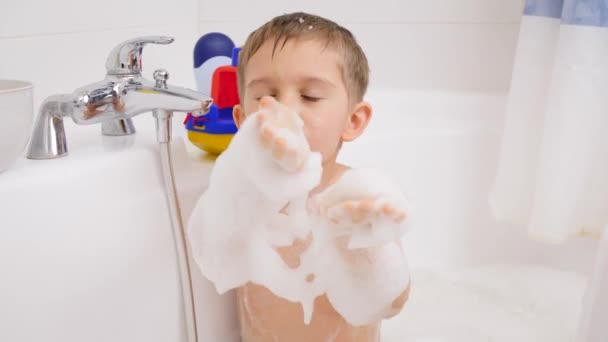 Funny little boy taking bath and playing with soap foam. Concept of child hygiene and health care at home. Kids having fun and playing - Footage, Video
