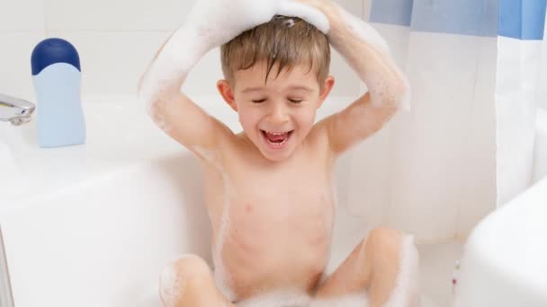 Mouvement lent d'heureux petit garçon drôle se lavant la tête avec un shampooing tout en prenant un bain à la maison. Concept d'hygiène infantile et de soins de santé à domicile. Les enfants s'amusent et jouent - Séquence, vidéo