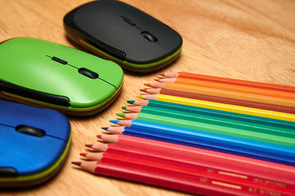 A closeup shot of multi-colored pencils and computer mouses on a wooden table - Fotoğraf, Görsel