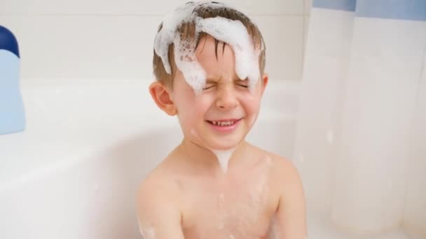 Mouvement lent de joyeux petit garçon jouant dans le bain et éclaboussant d'eau tout en se lavant la tête avec un shampooing. Concept d'hygiène infantile et de soins de santé à domicile. Les enfants s'amusent et jouent - Séquence, vidéo