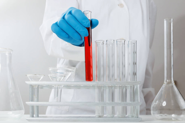In a chemical laboratory, a pharmacist man analyzes a test tube with red liquid. Medical experiment. A chemist is working on a test with protective gloves. - Photo, Image