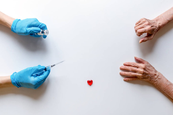 Ιατρική σύριγγα και φύσιγγα με φάρμακο στα χέρια ενός γιατρού με ιατρικά γάντια σε λευκό φόντο, τα απλωμένα χέρια μιας ηλικιωμένης γυναίκας - Φωτογραφία, εικόνα