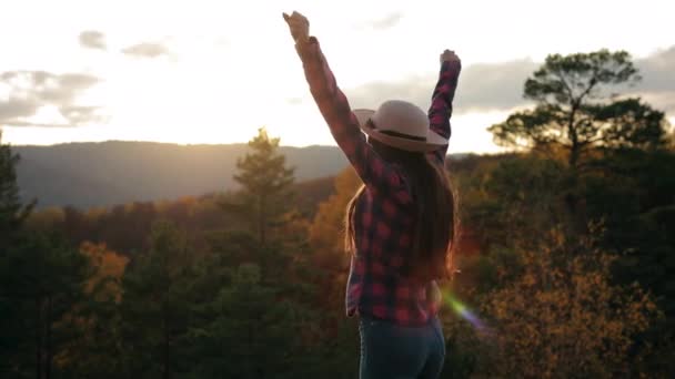 Een jonge vrouw staat op een klif en steekt haar handen in de lucht. Ze verheugt zich en springt. Wandelen in de bergen. 4K - Video