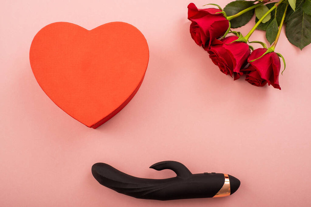 Flowers, black faloimitator on a pink background and a box in the form of a heart. Flat lay - Foto, imagen